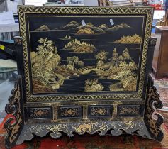 A Chinese black lacquered fire-screen with gilt painted scene of an Oriental landscape and motifs,