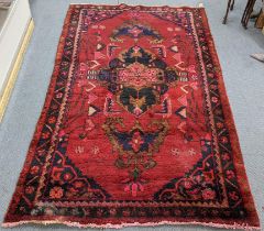 A Persian hand woven red ground rug having a central motif and repeating patterns, 260cm x 145cm