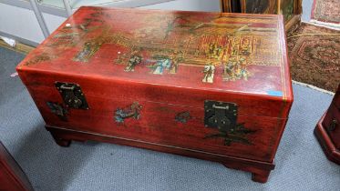 A late 20th century oriental style, red lacquered chest with a hinged top, decorated with a garden