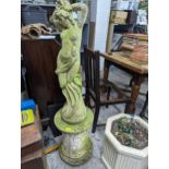 A weathered composition concrete garden statue of a semi clad woman on a circular plinth, floral