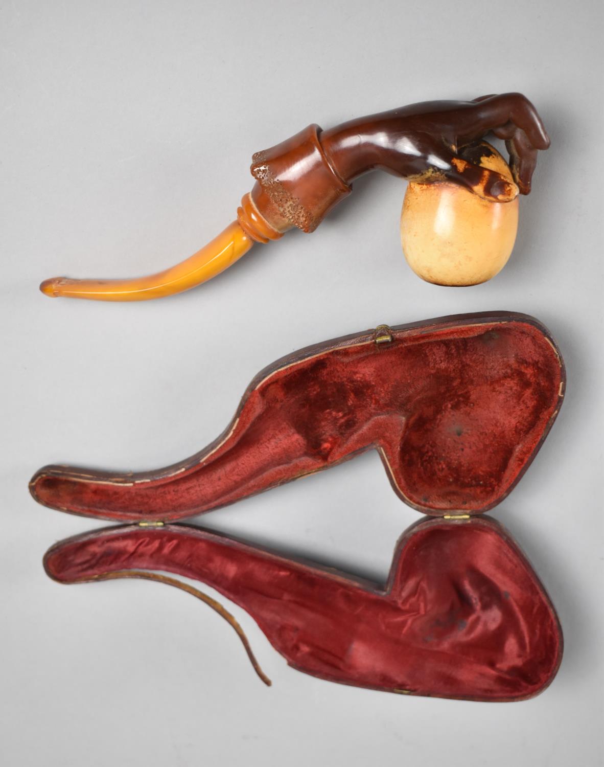A 19th Century Cased Amber and Meerschaum Pipe Modelled as a Hand Holding an Egg, 21cms Long