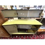 A 1950s/1960s YELLOW AND BLACK MELAMINE SIDEBOARD WITH SLIDING GLASS DOORS AND TWO CUPBOARDS.
