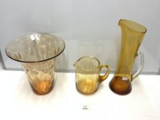 TWO AMBER WHITEFRIARS GLASS WATER JUGS, 36 CMS TALLEST, AND TRUMPET SHAPED AMBER GLASS VASE.