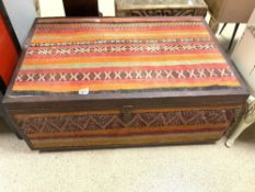 A MOROCCAN KELIM CARPET COVERED THE EASTERN STORAGE TRUNK, WITH LEATHER BORDERS, AND A METAL LOCK.