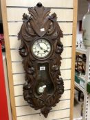 LATE VICTORIAN CARVED WALNUT AND EBONISED WALL CLOCK WITH CIRCULAR DIAL WITH BRASS PENDULUM BOB