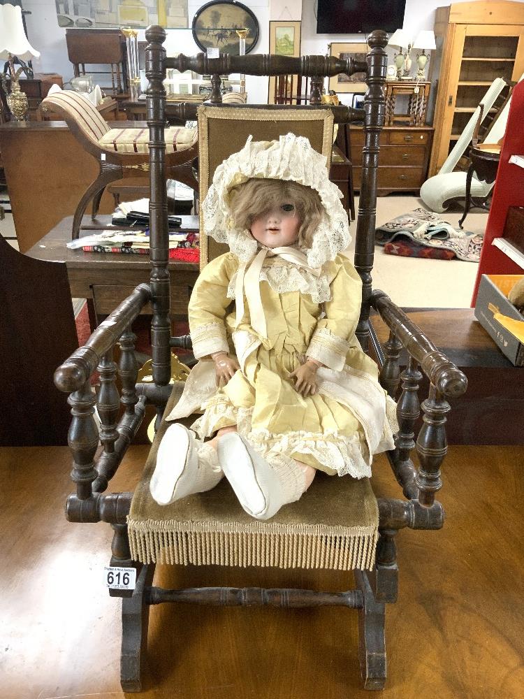 A CHILDS ANTIQUE AMERICAN ROCKING CHAIR WITH A BISQUE HEADED ARMAND MARSEILLE DOLL.