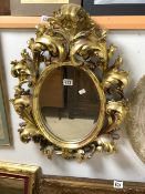 A ROCOCO STYLE GILT PAINTED COMPOSITE OVAL WALL MIRROR; 68X50 CMS.