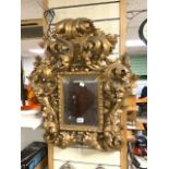 A 19TH-CENTURY HIGHLY ORNATE ROCOCO DESIGN GILT PAINTED BEVELLED WALL MIRROR; 75X70 CMS. (RE -