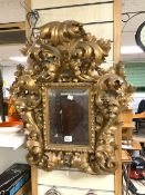 A 19TH-CENTURY HIGHLY ORNATE ROCOCO DESIGN GILT PAINTED BEVELLED WALL MIRROR; 75X70 CMS. (RE -