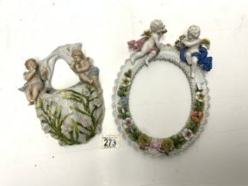 A CONTINENTAL PORCELAIN CHERUB MOUNTED OVAL PHOTO FRAME AND A PORCELAIN WALL POCKET.