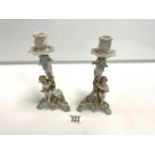 A PAIR OF CONTINENTAL PORCELAIN PUTTI AND FLORAL ENCRUSTED CANDLESTICKS; 23 CMS.