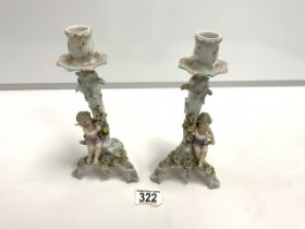 A PAIR OF CONTINENTAL PORCELAIN PUTTI AND FLORAL ENCRUSTED CANDLESTICKS; 23 CMS.