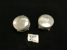 TWO HALLMARKED SILVER CIRCULAR RING BOXES, THE LIDS WITH MONOGRAMS, RAISED ON SCROLL SUPPORTS.