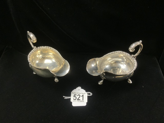 A PAIR OF GEORGE III HALLMARKED SILVER SAUCEBOATS WITH GADROONED RIMS AND SCROLL HANDLES ON HOOF