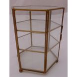 A hexagonal glass and gilded metal display case with two shelves, hinged door on four ball feet,