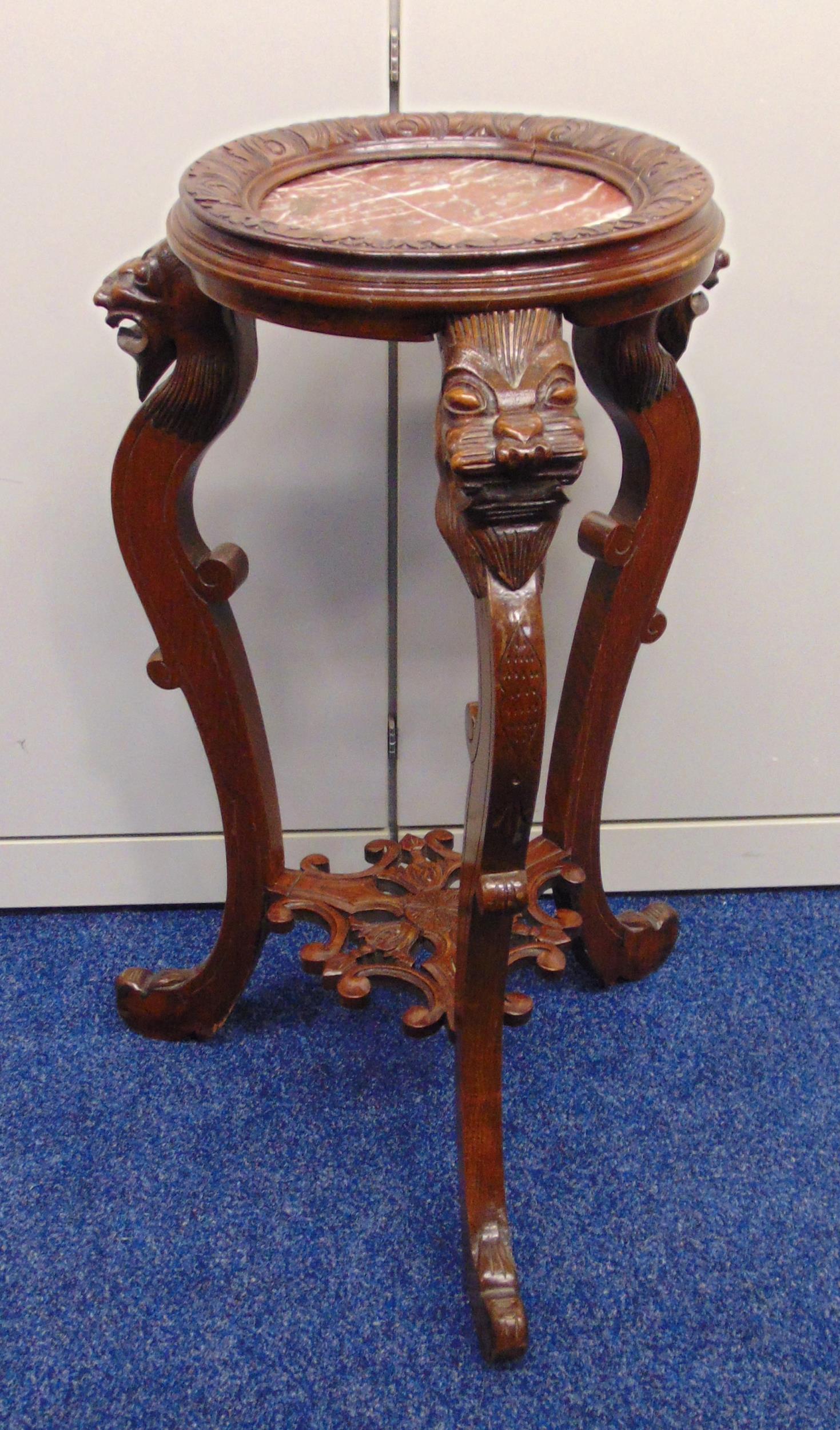 An oriental carved wooden plant stand with lion mask scroll legs supporting circular top with marble