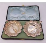 A cased set of hallmarked silver butter dishes, shaped circular with scroll and leaf chased sides