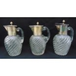 A set of three glass claret jugs with spirally fluted bodies and white metal collars and hinged