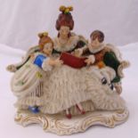 Dresden figural group of a lady and children seated on a couch reading a book, wearing classical