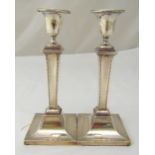 A pair of hallmarked silver table candlesticks, tapering rectangular stems with husk borders on