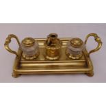 A brass two handled rectangular desk stand with two glass inkwells, a taper stick holder and a