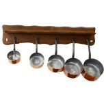 A graduated set of 5 French 1970s copper pans, with wooden hanging rack, largest pan diameter