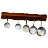 A graduated set of 5 French 1970s copper pans, with wooden hanging rack, largest pan diameter