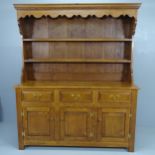 A reproduction oak two section dresser with boarded plate rack, three frieze drawers and cupboards