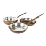 A set of 3 polished copper pans with iron handles, largest 30cm diameter, and a copper pan with