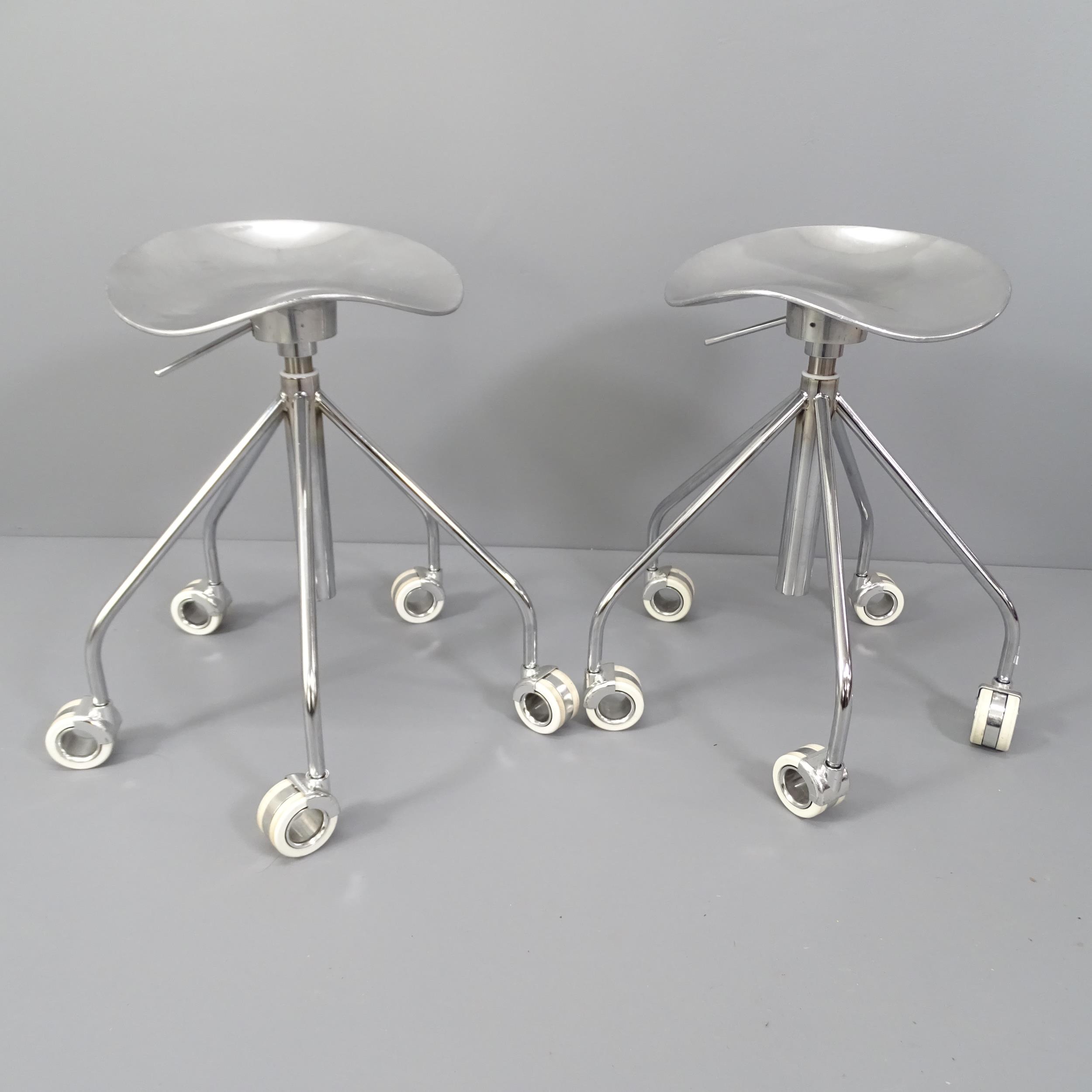 A pair of polished cast aluminium stools with gas height adjust on white hollow wheels.