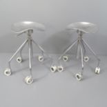 A pair of polished cast aluminium stools with gas height adjust on white hollow wheels.