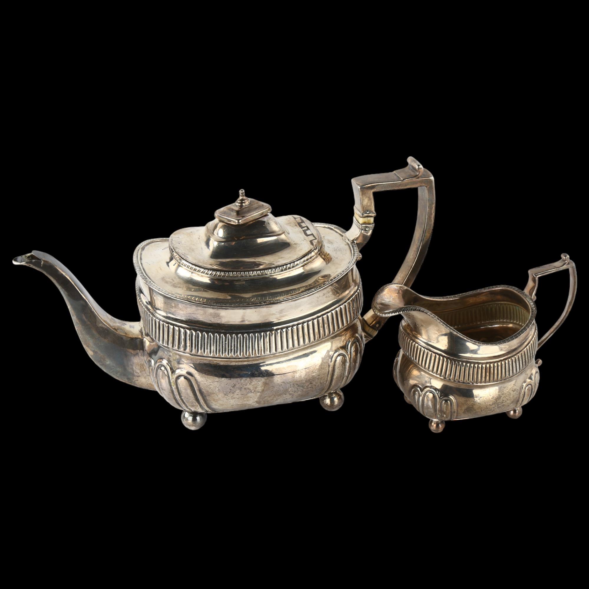 A George III silver teapot and cream jug set, oval bulbous form with half-fluted decoration,