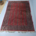 A red-ground Bokhara carpet. 280x190cm. Large tear to one edge. Some fringe loss. Various areas of