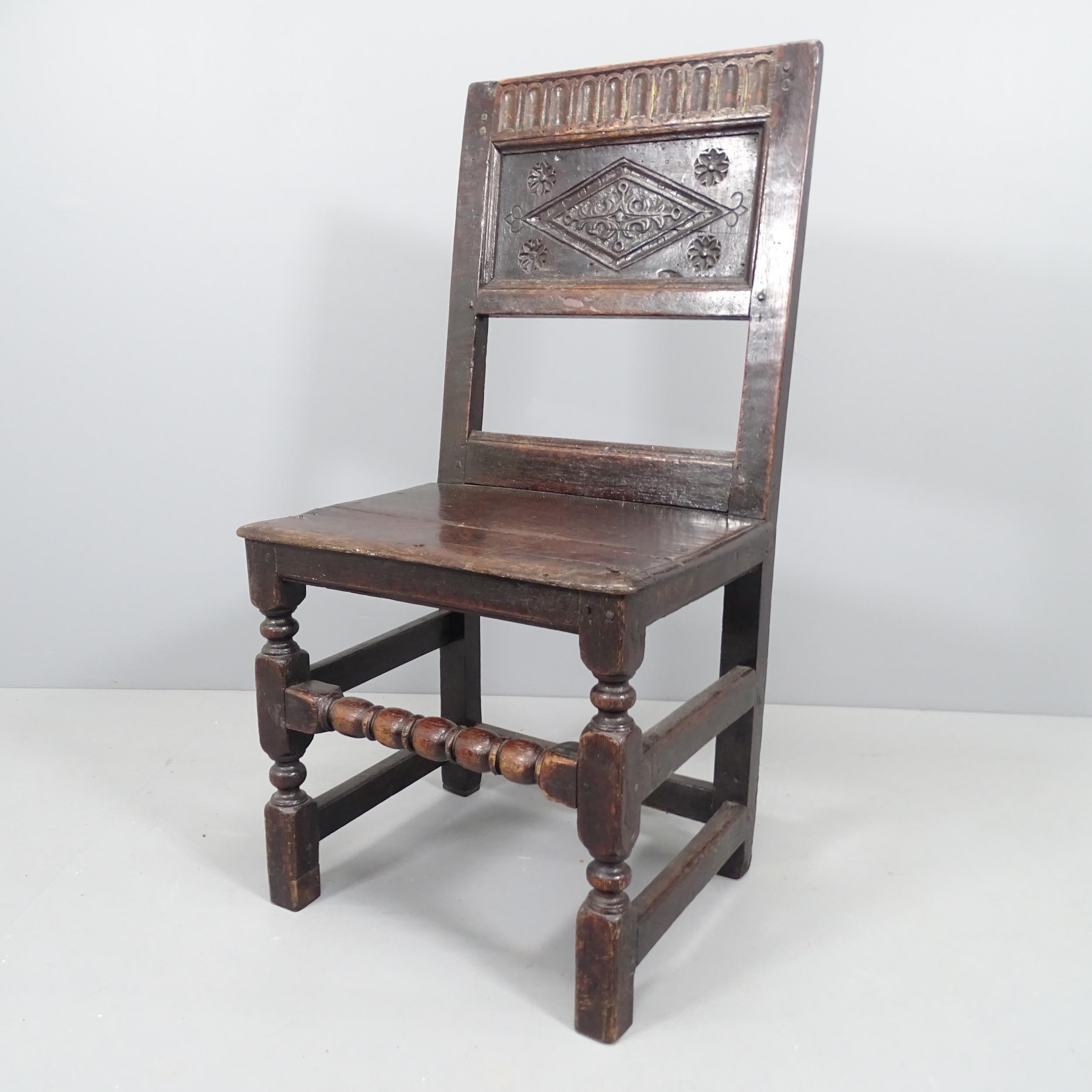 A 17th century and later panelled oak hall chair with carved back and turned stretcher.