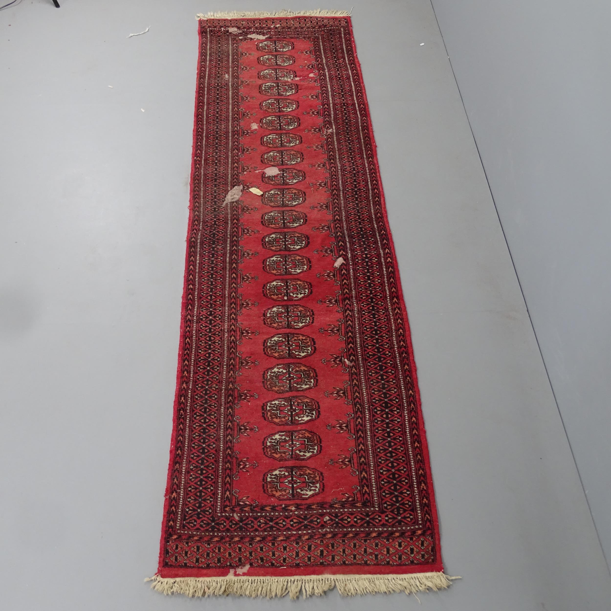 A red-ground Bokhara runner. 280x80cm Several damaged areas with severe pile loss. Faded.