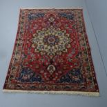 A red-ground Persian Sarouk rug. 202x138cm Repair at centre of rug. Some areas of pile loss and