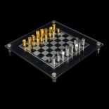 A Modernist hand turned steel and brass chess set, with glass chess board in original leather