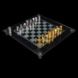 A Modernist hand turned steel and brass chess set, with glass chess board in original leather