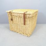 A large wicker basket with rope carry handle and leather straps. 64x52x64cm. 1 buckle missing for