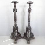 A pair of ebonised contintental torchere stands With carved decoration, tripod legs and platform