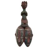 A West African carved and painted double face mask, surmounted by a fertility figure, L70cm
