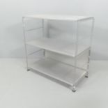 A contemporary designer three-tier shelving unit with perforated metal shelves on chrome steel base.