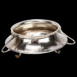 An Edward VII Arts and Crafts hammered circular silver fruit bowl, with 3 stylised handles on 3