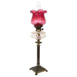 A brass Corinthian column oil lamp, with a frilled cranberry glass shade, H77cm