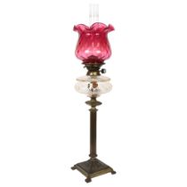 A brass Corinthian column oil lamp, with a frilled cranberry glass shade, H77cm