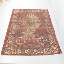 A red-ground Persian Bakhtiari rug. 205x160cm. In need of a clean. Threadbare to centre. Damage to