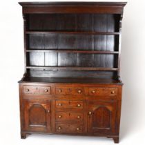 A George III Welsh oak dresser, with plate rack and fielded panelled doors with brass knob
