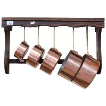 A graduated set of 5 copper bound and brass-handled pans, complete with an oak hanging rack