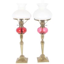A pair of Victorian brass oil lamps of tapered form, with milk glass shades and cranberry fonts,