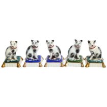 A group of Continental porcelain cat figurines, all cats seated on cushions of blue and green,